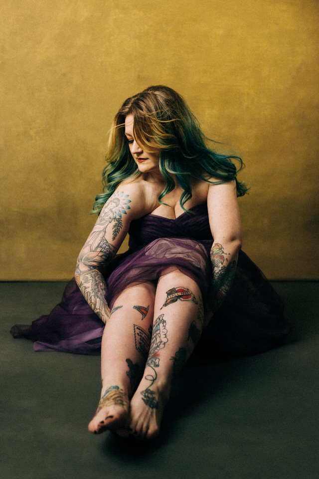 Colourful Boudoir image of a long haired woman sitting on the ground wearing a gown and featuring her tattoos