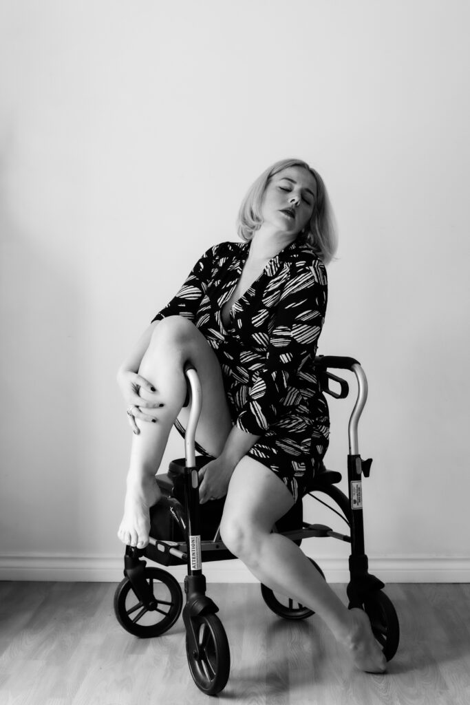Woman wearing a short dress sitting on a walker in a sexy pose with head flung to the back celebrating angio-iversary 