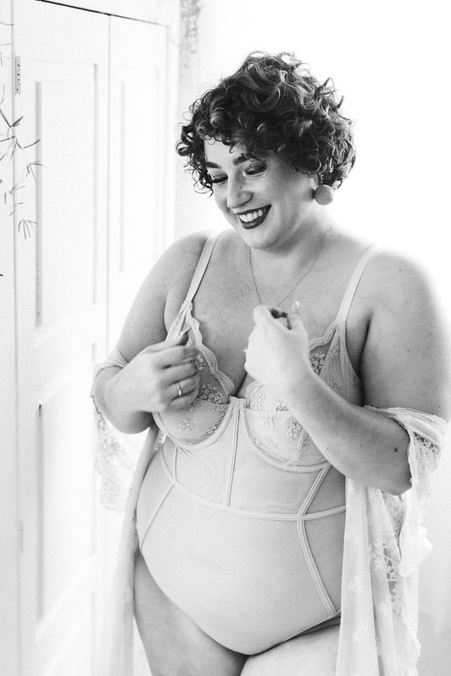 Woman wearing lingerie standing and laughing with a robe hanging around her elbows