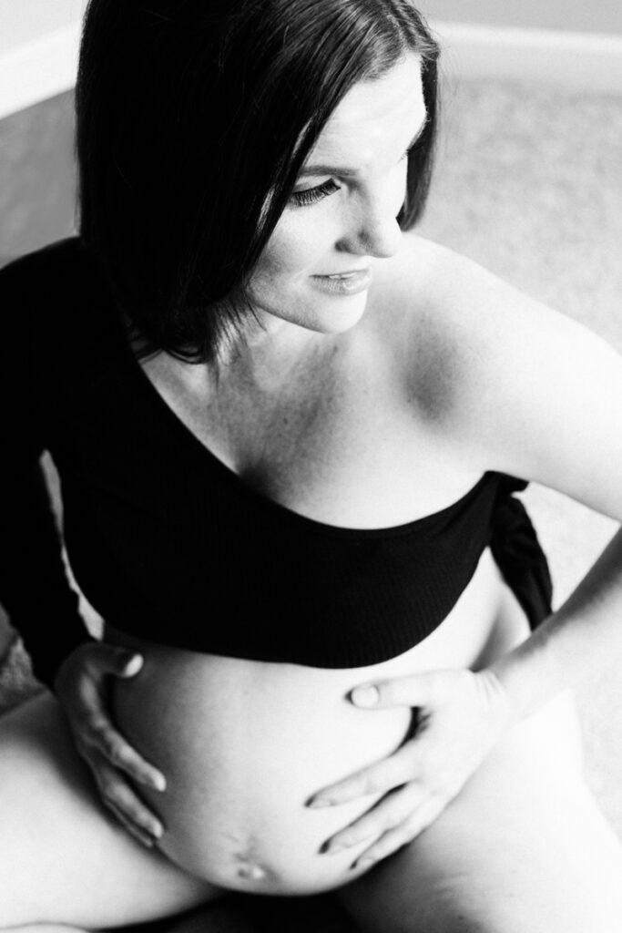 maternity boudoir photo of pregnant woman sitting on floor holding her bare belly