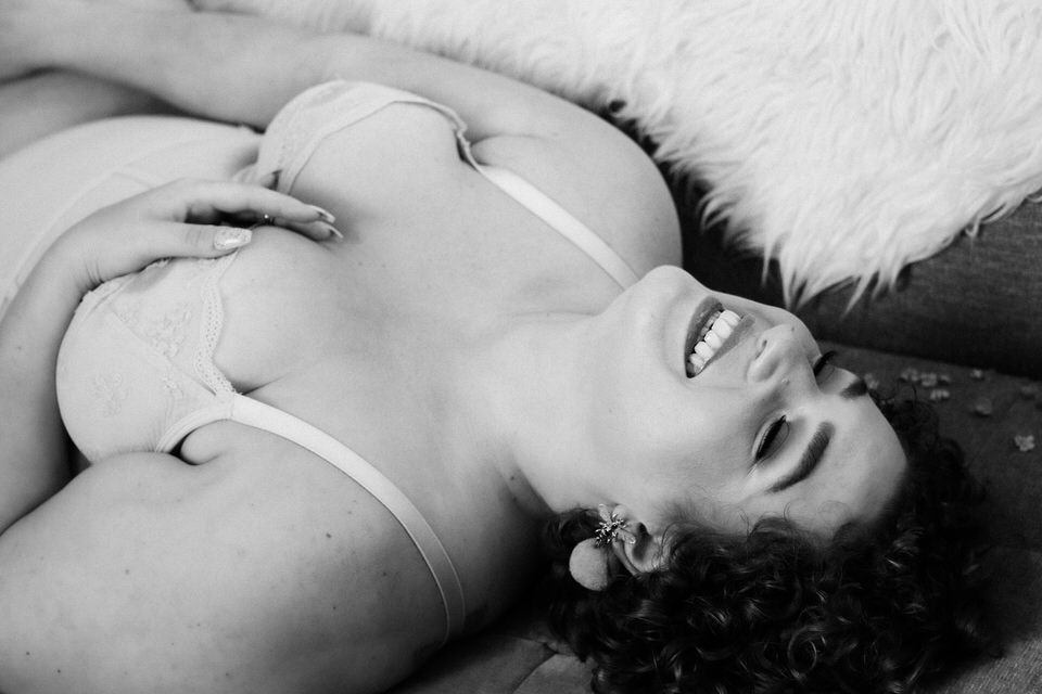 Woman in lingerie laying on her back laughing in boudoir photo