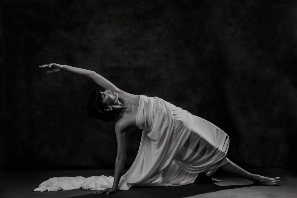Woman over 40 draped in a white sheet stretching gracefully in a yoga pose