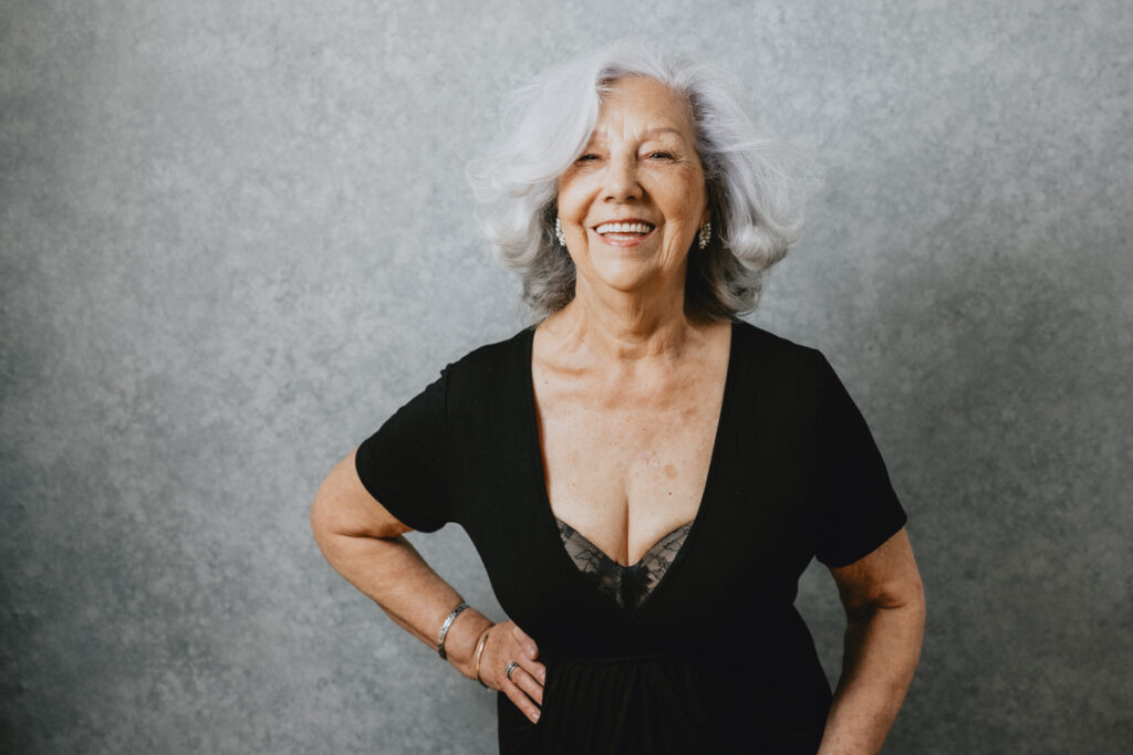 Woman with white hair wearing a low cut black dress is smiling and laughing