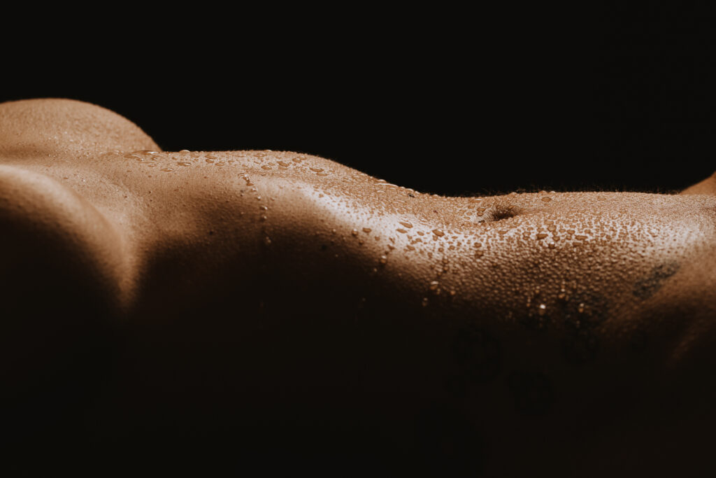 a luxe close up image of a woman's stomach, she's laying down and there's water drops on her body