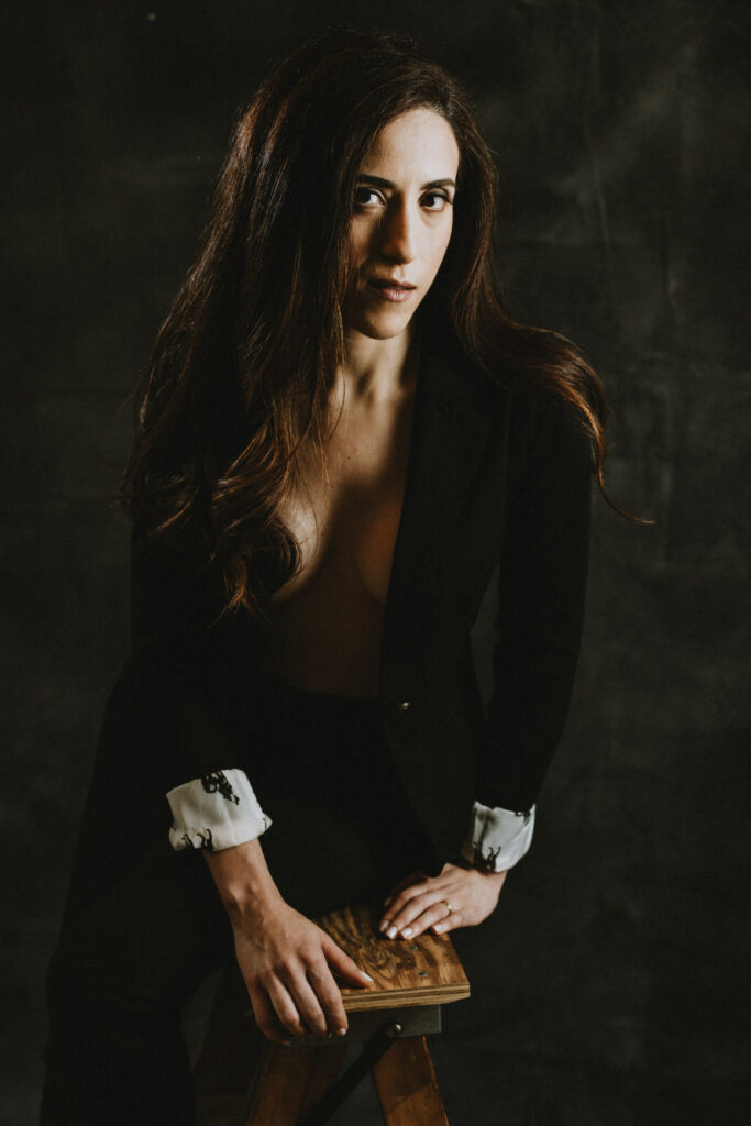 Woman in an open black suit jacket showing her cleavage, sitting atop of a ladder looking mysteriously in the camera, shot by a Vancouver Portrait Photographer
