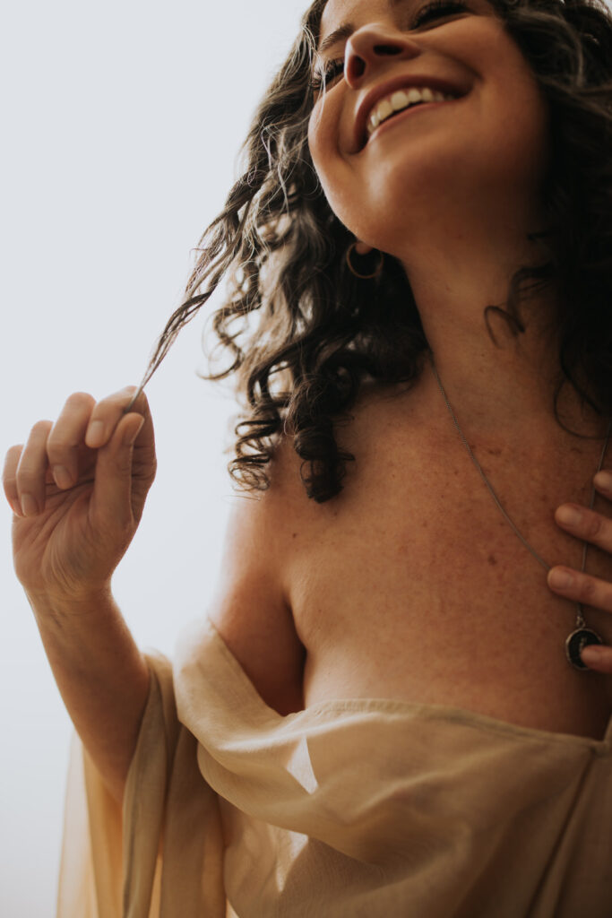 changing the ageing narrative one voice at a time. woman with sheer fabric draped over her elbow showing her shoulder and hand twirling her hair. Vancouver boudoir studio