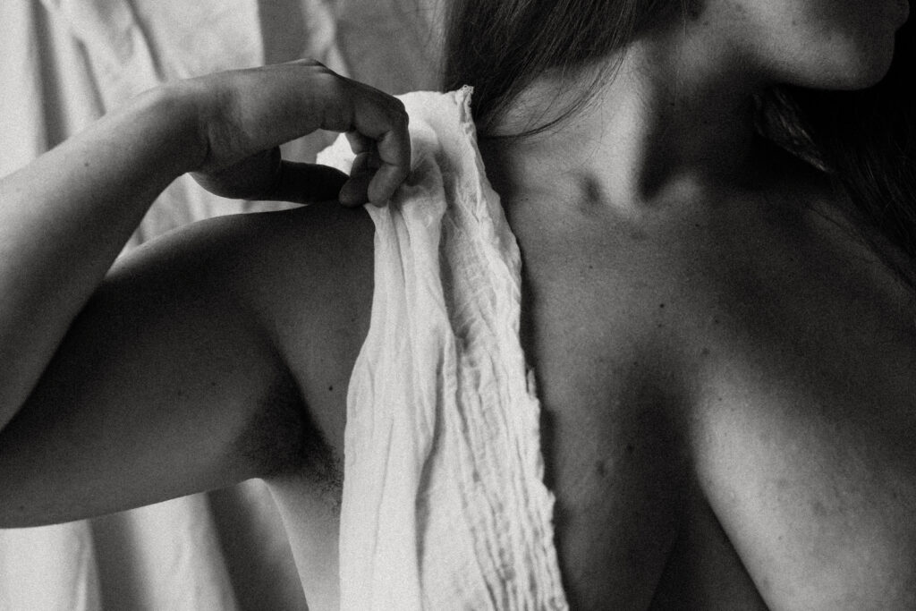 black and white boudoir image of woman's breasts, one covered by a cloth