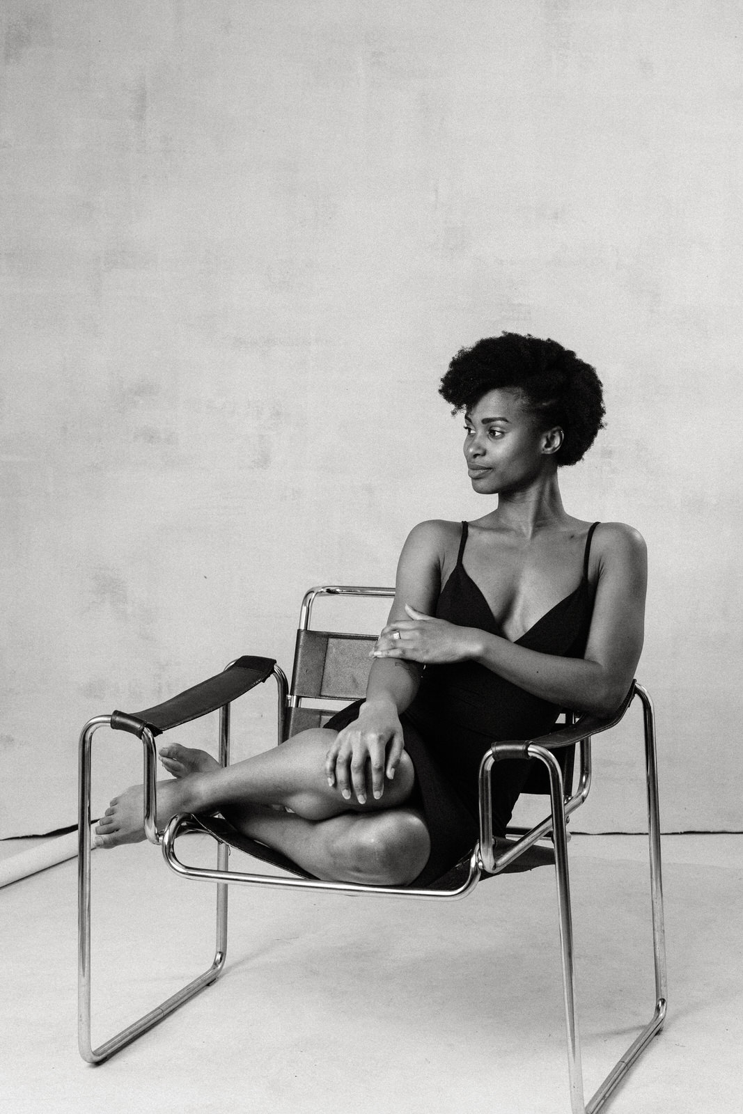 Black woman in contemporary boudoir portrait with simple elegant styling wearing a simple black dress sitting on a chair.