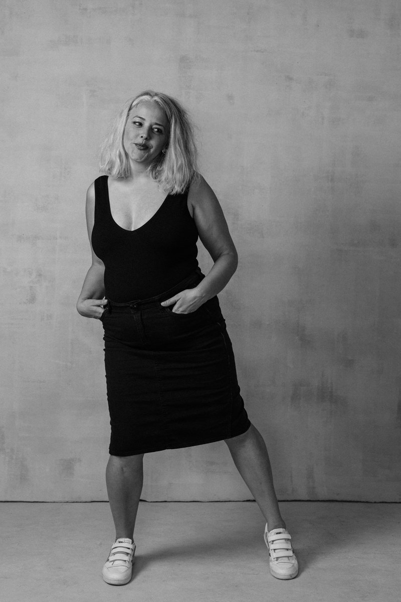 Black and white portrait of woman smiling while wearing a black dress with her hands tucked into her pockets