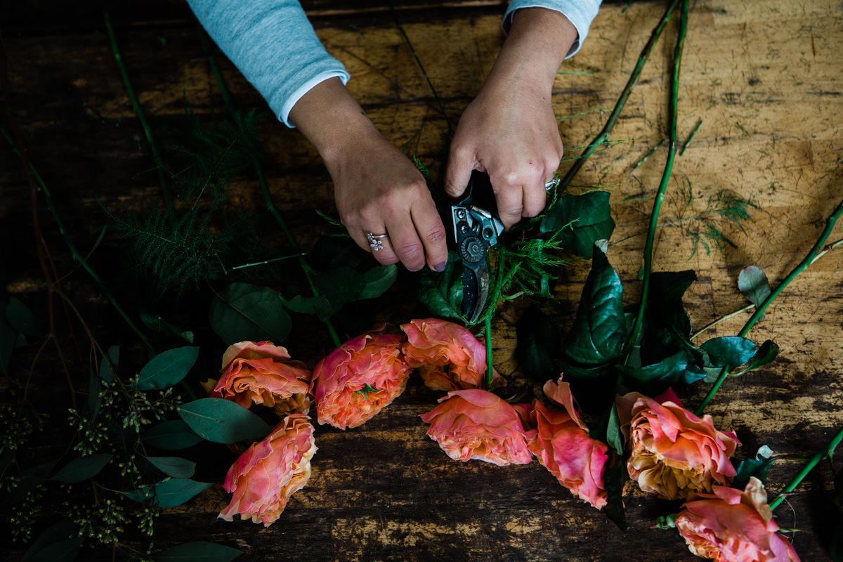 birds eye view of a florist trimming peonies on a wood surface. photo taken by vancouver photographer michele mateus
