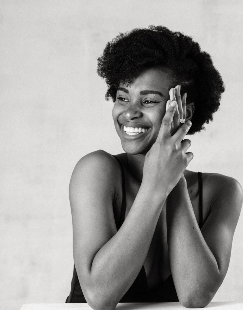 Vancouver boudoir editorial portrait of Black woman in contemporary minimalist styling smiling with hands held up to side of her face for photoshoot prep