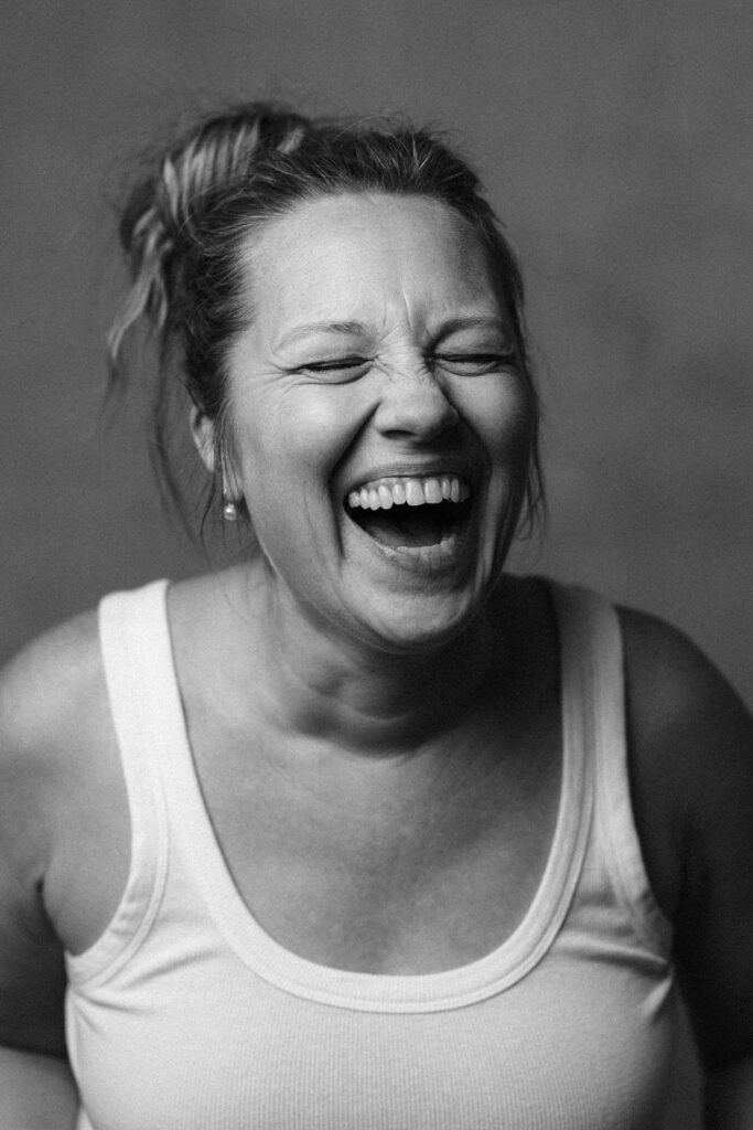 black and white image of a woman laughing, wearing a white tank top with a messy bun by vancouver photographer Michele Mateus